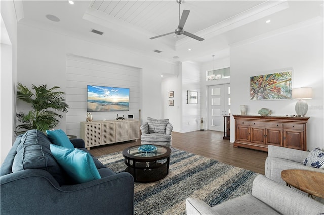 living room with crown molding, ceiling fan with notable chandelier, a tray ceiling, and dark wood-type flooring