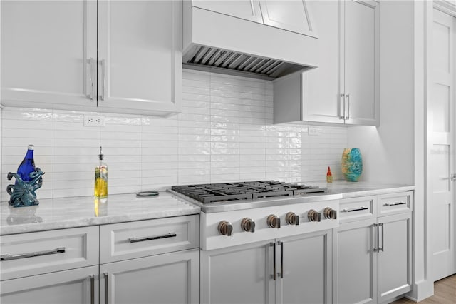 kitchen featuring decorative backsplash, light hardwood / wood-style floors, light stone counters, stainless steel gas stovetop, and extractor fan