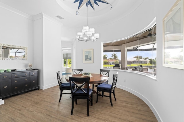 dining room featuring wood-type flooring, an inviting chandelier, a tray ceiling, and crown molding