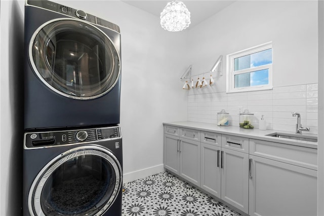 laundry area featuring stacked washer / dryer, a notable chandelier, sink, and cabinets