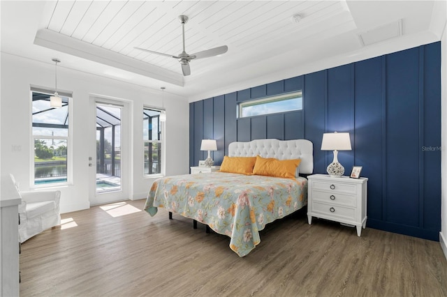 bedroom with ceiling fan, a tray ceiling, dark hardwood / wood-style floors, and access to outside