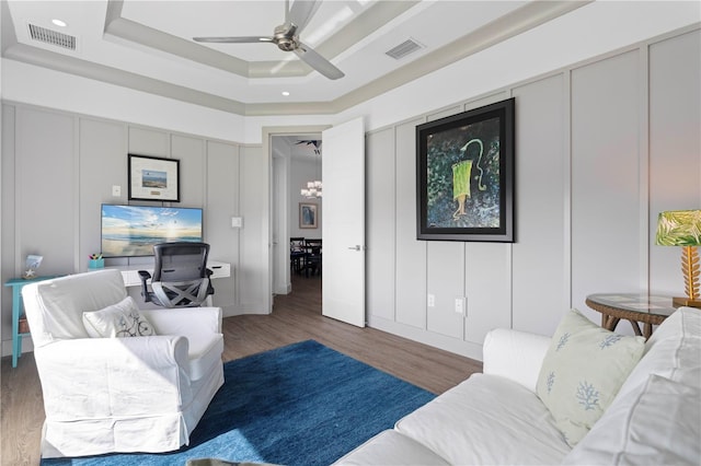 living room with ceiling fan with notable chandelier, hardwood / wood-style floors, and a raised ceiling