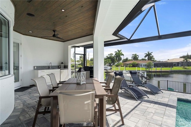 view of patio / terrace with ceiling fan, sink, a lanai, and a water view