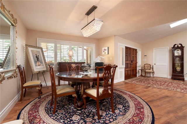 dining area with a healthy amount of sunlight, lofted ceiling with skylight, an inviting chandelier, and hardwood / wood-style flooring