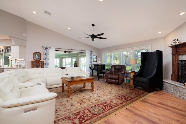 living room featuring ceiling fan, lofted ceiling, a premium fireplace, and light hardwood / wood-style floors