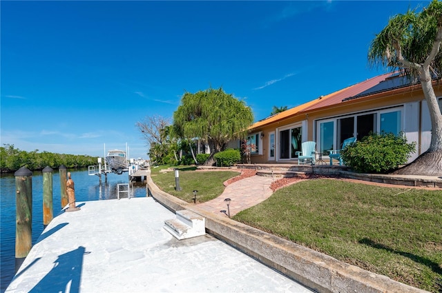 view of dock with a patio, a lawn, and a water view