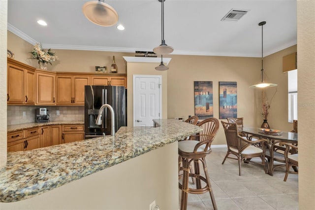 kitchen featuring decorative backsplash, stainless steel fridge, a kitchen breakfast bar, crown molding, and hanging light fixtures