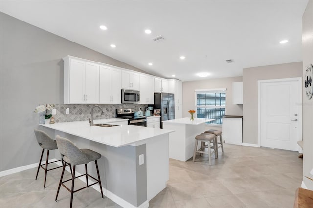 kitchen with sink, kitchen peninsula, appliances with stainless steel finishes, a breakfast bar area, and vaulted ceiling