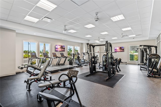 exercise room with a drop ceiling, ceiling fan, and plenty of natural light