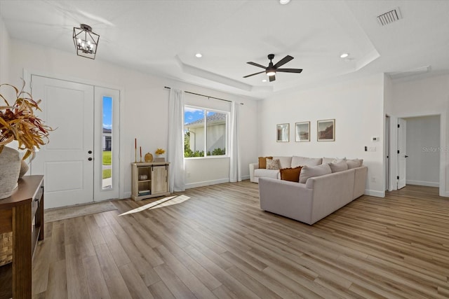 unfurnished living room with light hardwood / wood-style flooring, a tray ceiling, and ceiling fan with notable chandelier