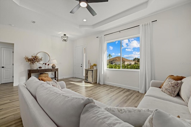 living room featuring a raised ceiling, ceiling fan, and light hardwood / wood-style flooring