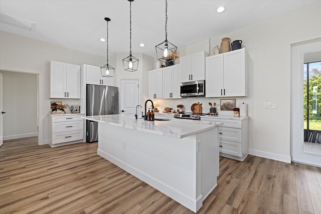 kitchen with white cabinets, stainless steel appliances, light hardwood / wood-style flooring, a kitchen island with sink, and sink