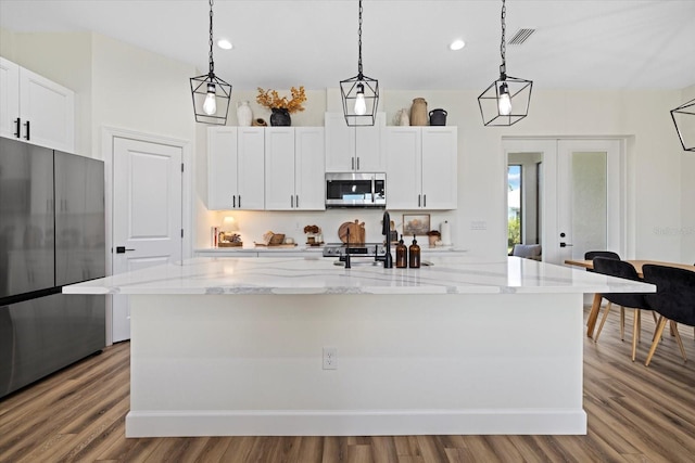 kitchen with an island with sink, light hardwood / wood-style floors, appliances with stainless steel finishes, and pendant lighting