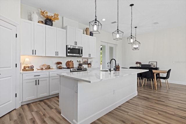 kitchen with white cabinets, hanging light fixtures, a center island with sink, light hardwood / wood-style flooring, and appliances with stainless steel finishes