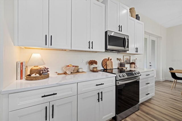 kitchen with light wood-type flooring, stainless steel appliances, and white cabinets