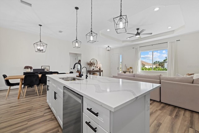 kitchen featuring a raised ceiling, dishwasher, an island with sink, and decorative light fixtures