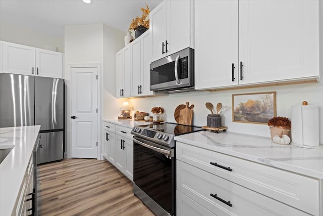 kitchen with light stone countertops, appliances with stainless steel finishes, light hardwood / wood-style floors, and white cabinetry