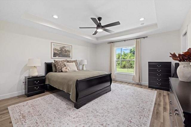 bedroom featuring ceiling fan, light wood-type flooring, and a raised ceiling