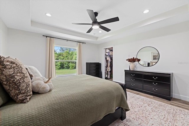 bedroom with ceiling fan, a closet, a tray ceiling, a spacious closet, and light wood-type flooring