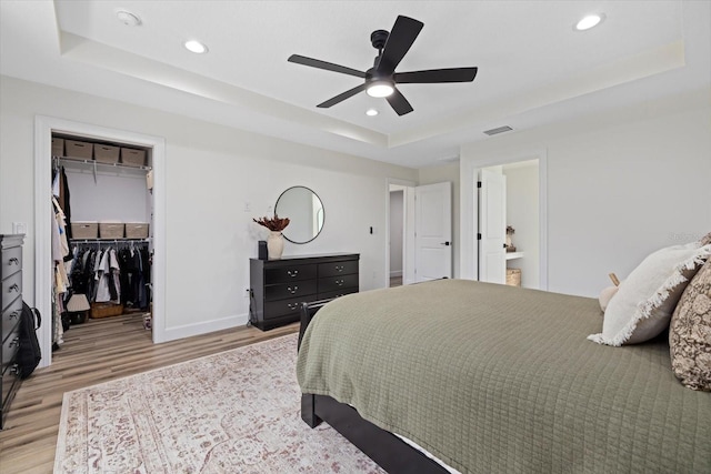 bedroom with ceiling fan, light wood-type flooring, a tray ceiling, and a spacious closet