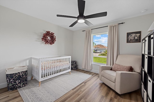 bedroom featuring wood-type flooring, ceiling fan, and a nursery area