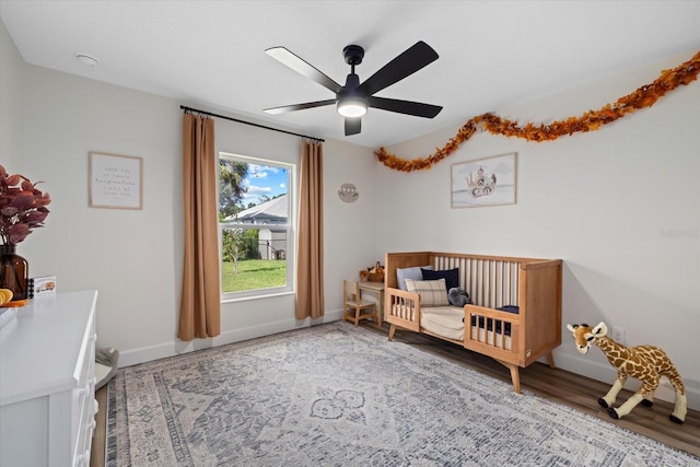 bedroom featuring ceiling fan, a nursery area, and wood-type flooring