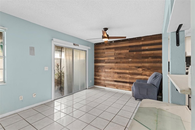 sitting room with wood walls, a textured ceiling, light tile patterned floors, and ceiling fan