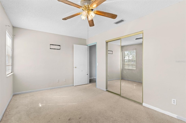 unfurnished bedroom with light carpet, a closet, a textured ceiling, and ceiling fan