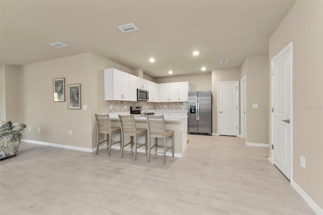 kitchen featuring tasteful backsplash, a breakfast bar, white cabinetry, stainless steel appliances, and a center island