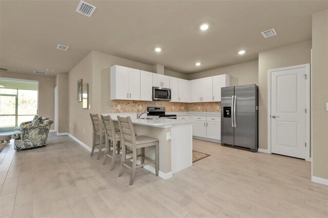 kitchen featuring stainless steel appliances, light hardwood / wood-style floors, kitchen peninsula, white cabinetry, and a kitchen bar