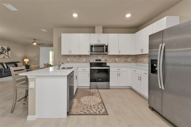 kitchen featuring light hardwood / wood-style floors, a breakfast bar area, kitchen peninsula, appliances with stainless steel finishes, and white cabinetry