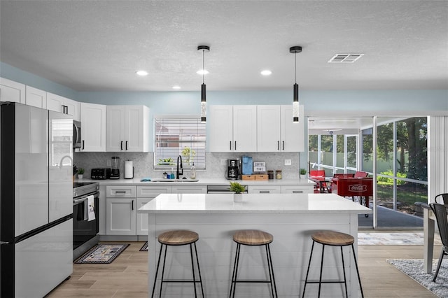 kitchen with white cabinets, hanging light fixtures, appliances with stainless steel finishes, a center island, and light wood-type flooring