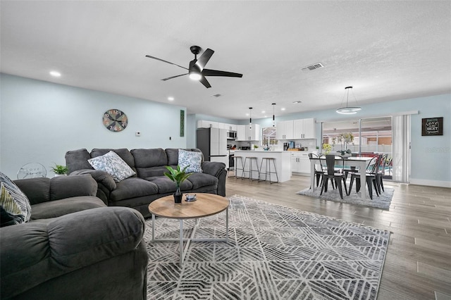 living room with light wood-type flooring, a textured ceiling, and ceiling fan