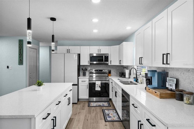 kitchen with hanging light fixtures, sink, white cabinetry, appliances with stainless steel finishes, and light hardwood / wood-style floors