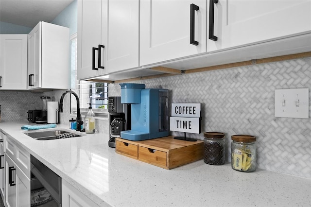 kitchen with light stone countertops, white cabinetry, backsplash, and sink