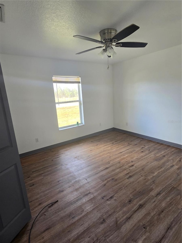 empty room featuring ceiling fan, dark wood-type flooring, and a textured ceiling