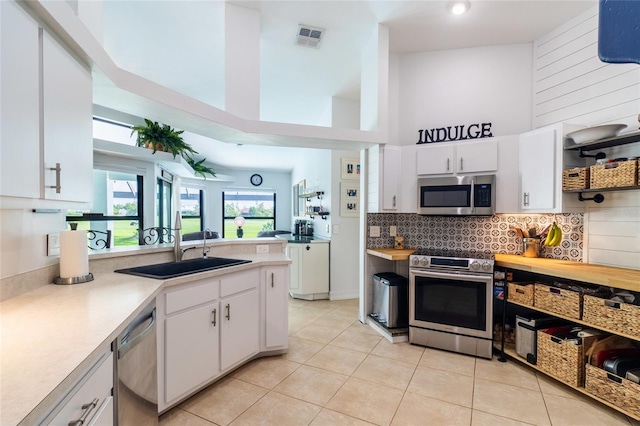 kitchen with light tile patterned floors, sink, white cabinetry, appliances with stainless steel finishes, and a towering ceiling