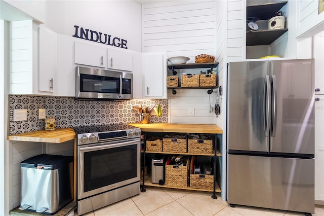 kitchen with light tile patterned floors, tasteful backsplash, white cabinetry, stainless steel appliances, and butcher block counters