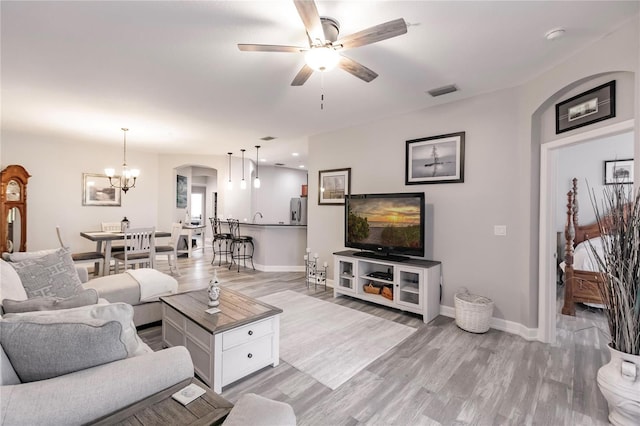 living room featuring ceiling fan with notable chandelier and light hardwood / wood-style flooring