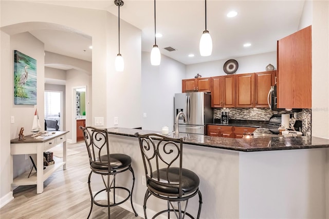 kitchen featuring kitchen peninsula, dark stone countertops, decorative light fixtures, and stainless steel appliances