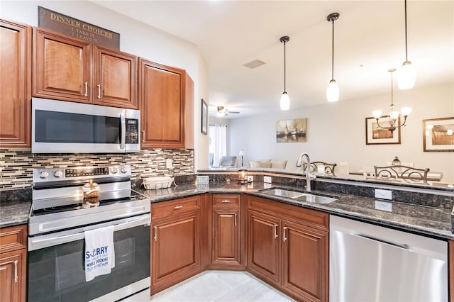 kitchen with appliances with stainless steel finishes, pendant lighting, dark stone counters, and sink