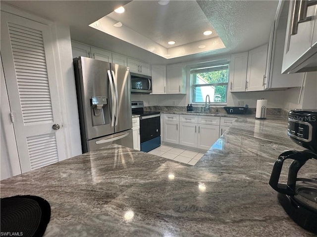 kitchen featuring white cabinetry, stainless steel appliances, dark stone counters, and a raised ceiling