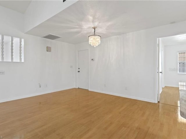 empty room with a notable chandelier and light wood-type flooring