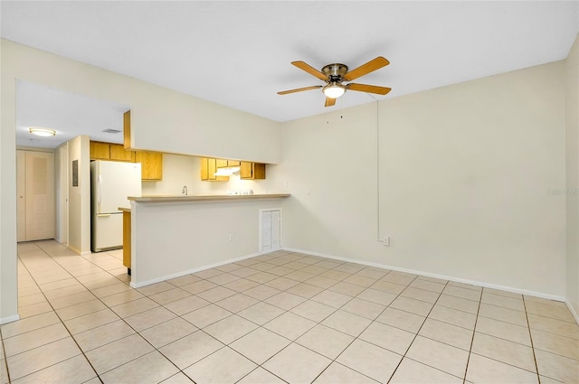 interior space featuring kitchen peninsula, light tile patterned floors, white fridge, and ceiling fan