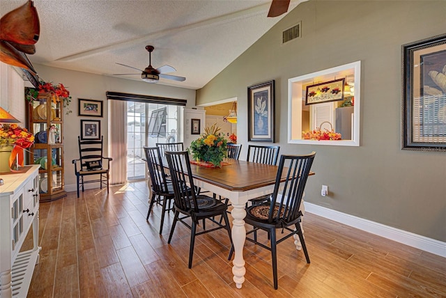 dining room featuring light hardwood / wood-style flooring, vaulted ceiling, a textured ceiling, and ceiling fan