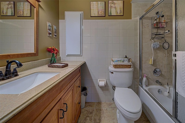 full bathroom with tile walls, toilet, vanity, and bath / shower combo with glass door