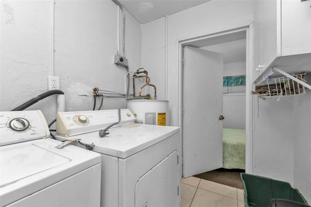 clothes washing area featuring electric water heater, cabinets, light tile patterned floors, and washing machine and dryer