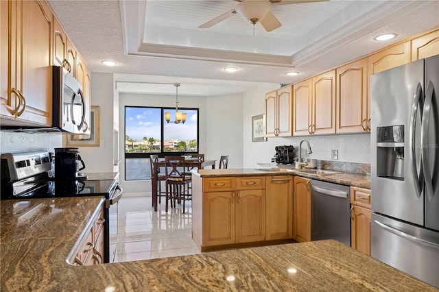 kitchen featuring dark stone counters, a tray ceiling, appliances with stainless steel finishes, and decorative light fixtures