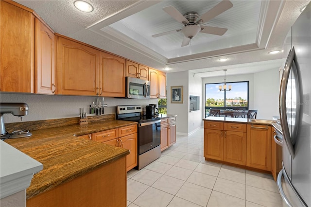 kitchen with ceiling fan with notable chandelier, kitchen peninsula, a raised ceiling, appliances with stainless steel finishes, and decorative light fixtures