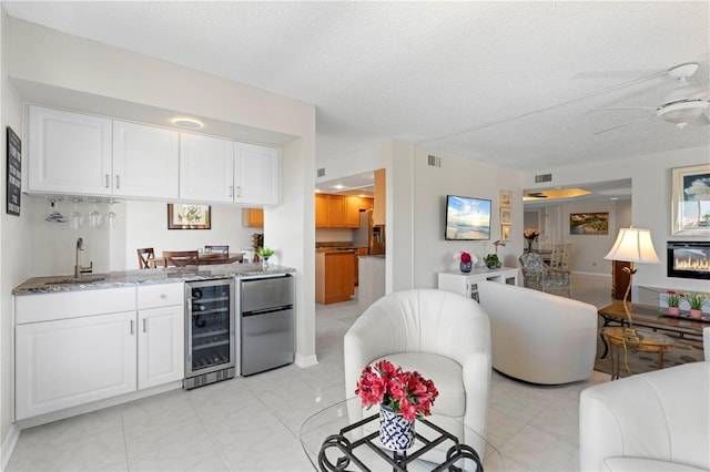 kitchen with a textured ceiling, beverage cooler, white cabinets, light stone countertops, and ceiling fan